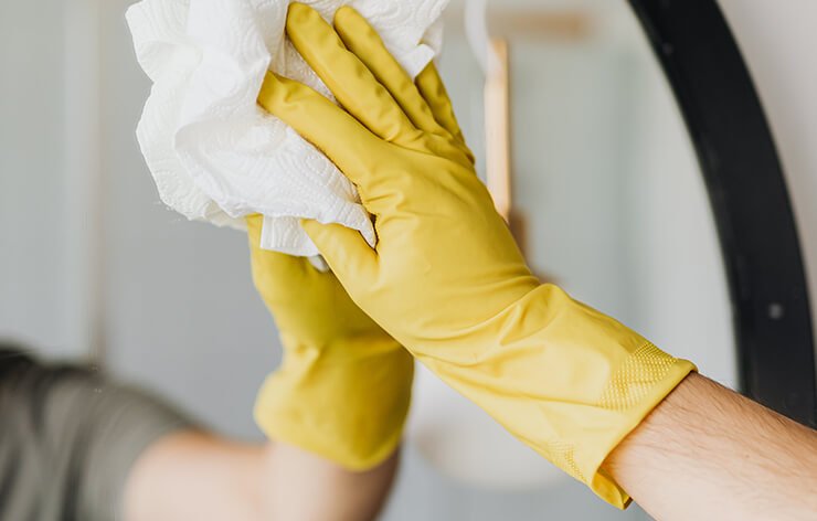 A man's hand with yellow gloves cleaning a mirror.